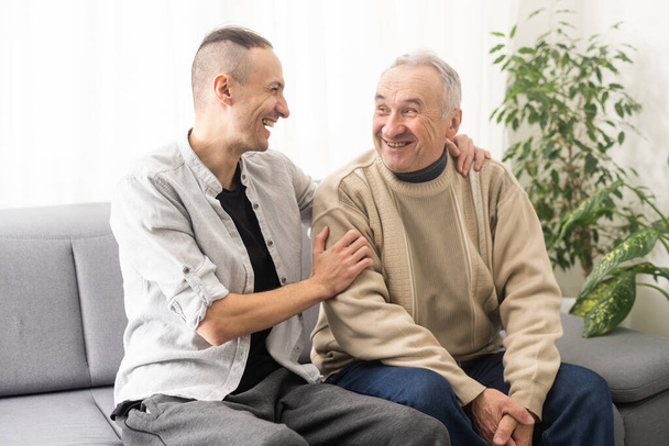Young adult caucasian son listening and supporting his old elderly senior father at home indoors. Care and love concept - Fotoğraf, Görsel