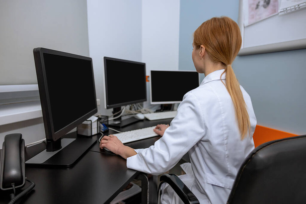 Laboratuvar önlüğü giyen profesyonel bilim kadını doktor malzeme odasındaki kişisel bilgisayarlarda çalışan monitörlerle çevrili.. - Fotoğraf, Görsel