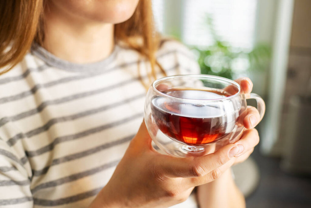 A nők kezei egy csésze forró teát tartanak reggel. Fiatal nő pihentető csésze tea kéznél. Jó reggelt, teafogalom. - Fotó, kép