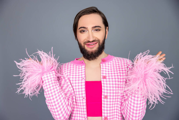 Joyful optimistic confident transgender person wearing pink clothing raised arms, being in good mood, posing isolated over gray background - Foto, Bild