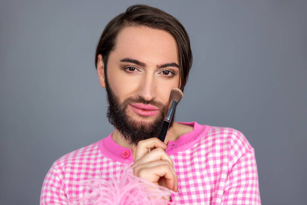 Beautiful transgender person model wearing pink clothing person applying powder on face preparing for photo session posing isolated over gray background - Valokuva, kuva