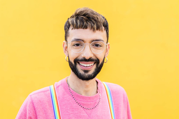 黄色の背景の上にカメラを見ている若い陽気なひげを生やしたゲイの男の笑顔の肖像画。LGTBQ人のコンセプト - 写真・画像