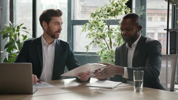 Two diverse multiracial businessmen signing document agreement shaking hands success business deal. Multiethnic men partners in office meeting handshake satisfied agree sign loan investment contract - Footage, Video