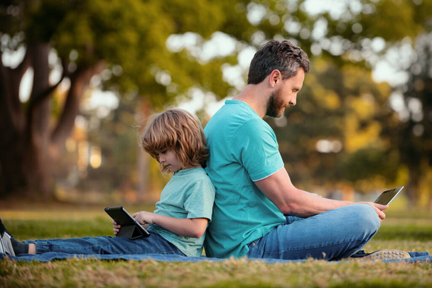 Un chico con papá aprendiendo la lección. Padre e hijo usan laptop, papá y el niño de la escuela mirando tableta. Aprendizaje a distancia - Foto, Imagen