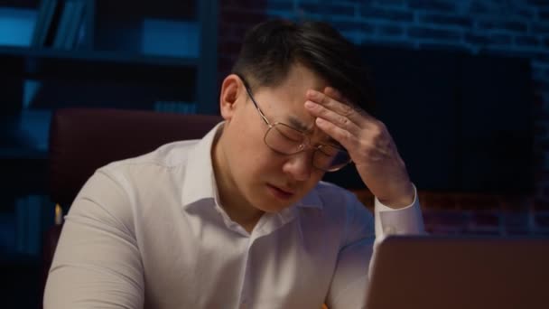 Estresado hombre de negocios asiático en gafas que trabajan con el ordenador portátil por la noche en casa oficina agotado enfermo cansado coreano de mediana edad hombre sobrecargado de trabajo ejecutivo sentir dolor de cabeza migraña estrés negocio fracaso - Metraje, vídeo