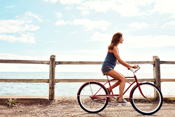 A fitnesz egy életstílus. egy gyönyörű fiatal nő biciklizik a sétányon. - Fotó, kép