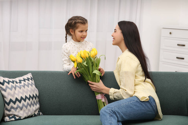 Daughter gifting happy woman bouquet of yellow tulips at home. Mother's day celebration - Fotoğraf, Görsel