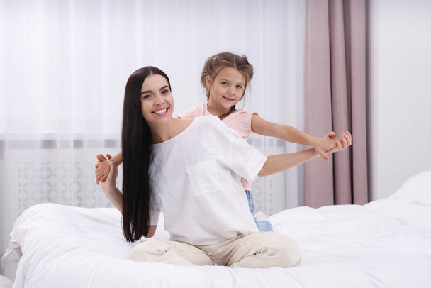 Happy woman and her daughter having fun on bed at home. Mother's day celebration - 写真・画像