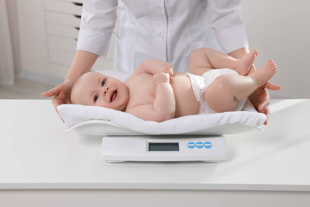 Pediatrician weighting cute little baby in clinic, closeup - Foto, Imagen