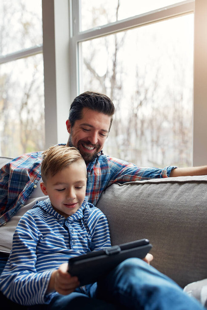 Tan joven, pero ya sabe mucho. un niño pequeño usando una tableta digital con su padre en casa - Foto, Imagen
