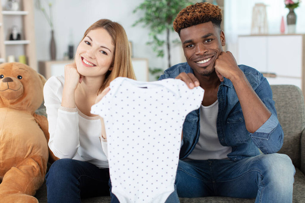 mixed couple showing baby cloths - Foto, Imagen