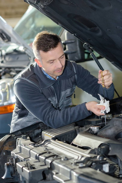 Специалист по автомобилестроению регулирует двигатель в своем гараже
 - Фото, изображение