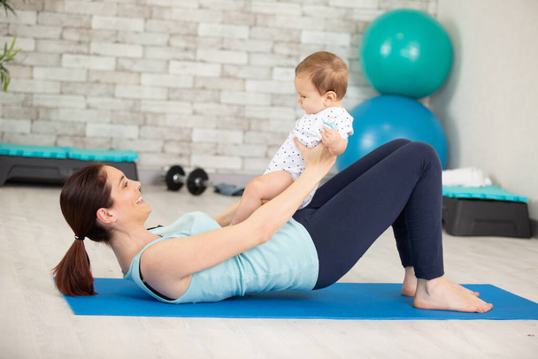 woman exercising with baby on mat on the floor - Фото, зображення