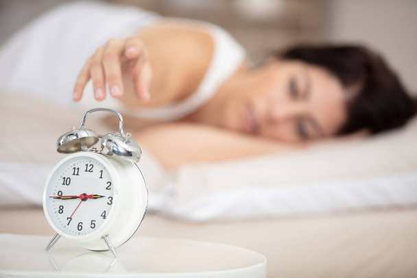 woman in bed reaching hand towards alarm-clock - Foto, Bild