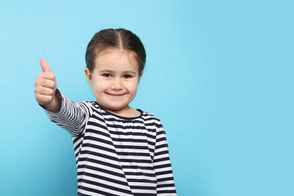 Happy girl showing thumbs up on light blue background. Space for text - Photo, image