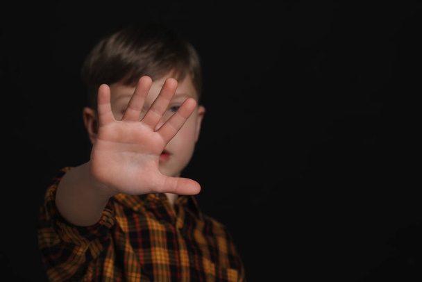 Boy making stop gesture against black background, focus on hand and space for text. Children's bullying - Фото, изображение
