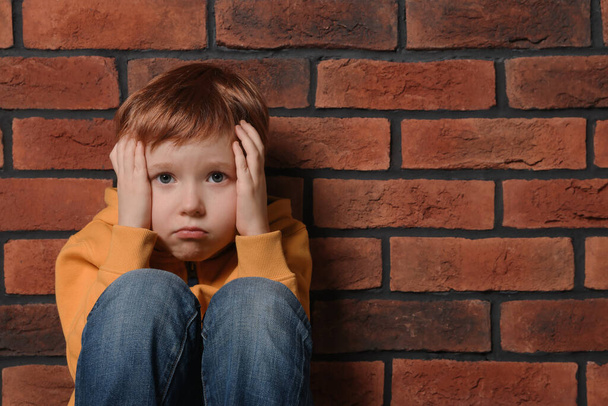 Zdenerwowany chłopak siedzący przy ścianie z cegły, miejsce na tekst. znęcanie się nad dziećmi - Zdjęcie, obraz