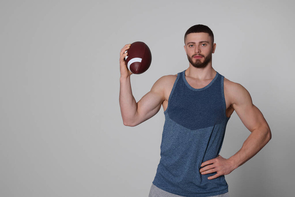 Athletic young man with American football ball on light grey background. Space for text - Foto, imagen