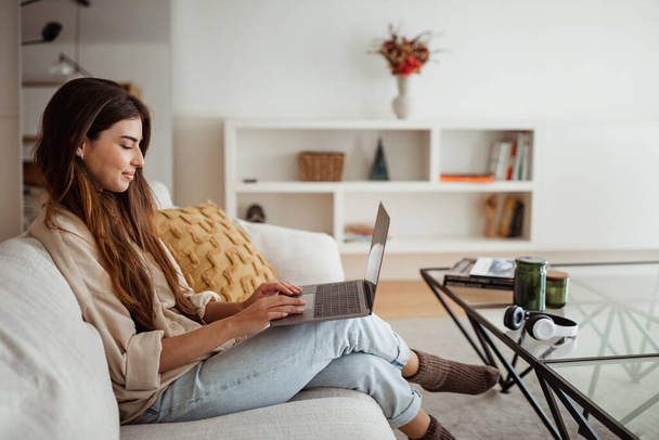 Remotely study, online lesson and gadget. Glad millennial european lady typing on computer in minimalist living room interior, profile. Freelance, work and business at home - Foto, Imagem