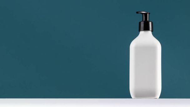 A white dispenser with cosmetics on a white shelf with a place for a logo on a dark blue background. The concept of routine body and hair care. Banner. Copy space - Valokuva, kuva