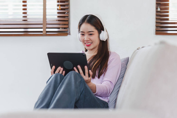 Aantrekkelijke Aziatische vrouw rust comfortabele woonkamer en met behulp van digitale tablet, Relax, Bank, Lifestyle. - Foto, afbeelding