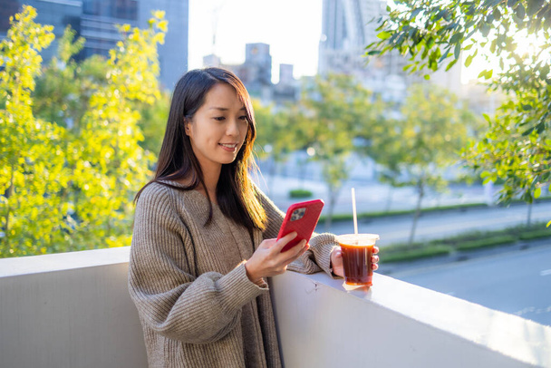Mujer uso de teléfono móvil con su café en la azotea bajo el atardecer - Foto, Imagen