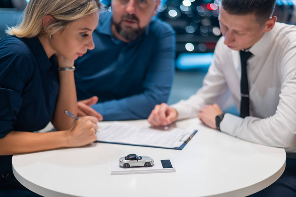 Happy caucasian couple signs a contract for the purchase of a car salon - Foto, Imagen