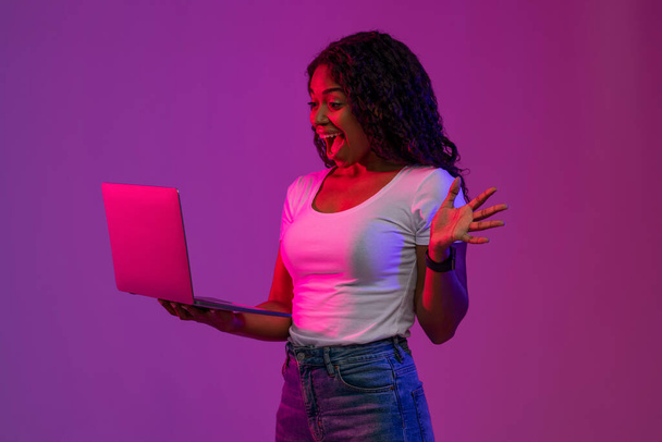 Cool Website. Portrait Of Excited Black Woman With Laptop In Hands Under Neon Lighting, Overjoyed African American Lady Celebrating Success With Laptop, Standing Over Purple Studio Background - Фото, изображение