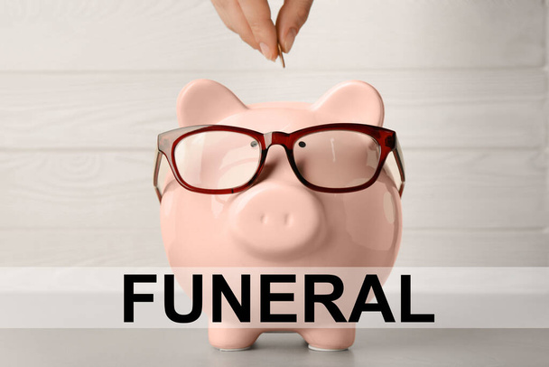 Money for funeral expenses. Woman putting coin into piggy bank at light grey table, closeup - Fotoğraf, Görsel