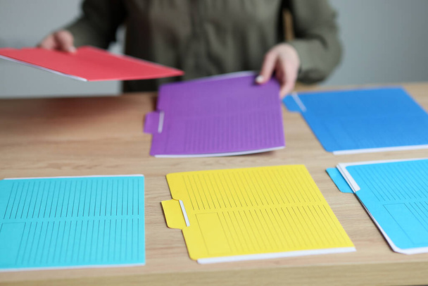 Secrétaire détaille les dossiers multicolores avec les documents comptables sur la table en bois. Femme trie des matériaux avec des données sur le lieu de travail dans le bureau - Photo, image