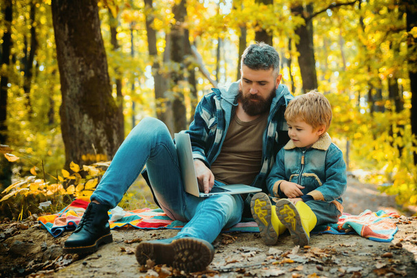 Man bearded father and little son with laptop in forest. Ecology upbringing. Father teaches son use modern technology. United with nature. Ecology lesson. Forest school and ecology education. - Фото, зображення