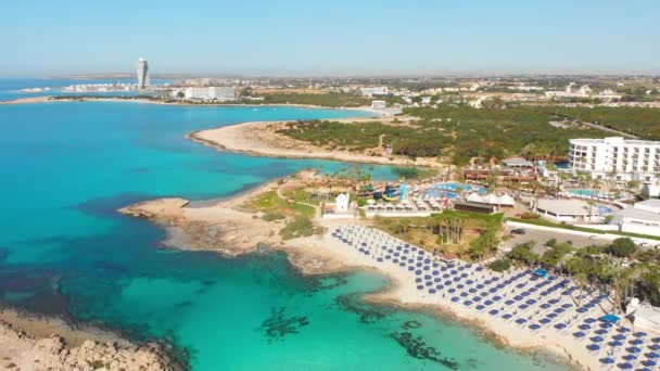 Ayia Napa, Cyprus - 15th april, 2023: aerial fly over Luxury hotel buildings with pools by beach with island greenery panorama. White sand most famous in Cyprus - Nissi beach - Footage, Video