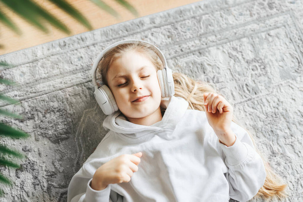 Smiling little girl listening music lying on the floor - Foto, Imagen