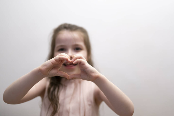A girl, a brunette of seven years, shows the figure of a heart with her hands. High quality photo - Φωτογραφία, εικόνα