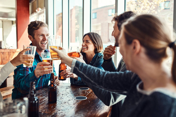 Tomando una pinta en el bar con amigos. un grupo de amigos haciendo un brindis mientras disfrutan en un bar - Foto, imagen