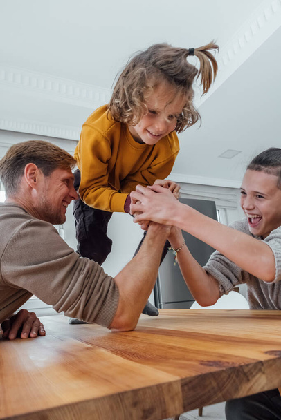 Father competing in arm wrestling with teenager son, family spending time together. Dad and children having fun at home.  - Photo, Image