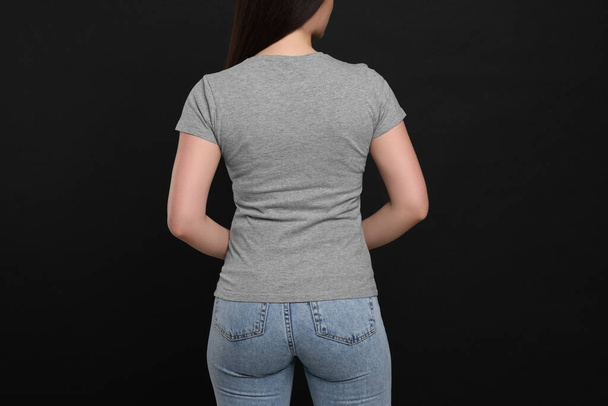 Woman wearing grey t-shirt on black background, back view - Foto, immagini
