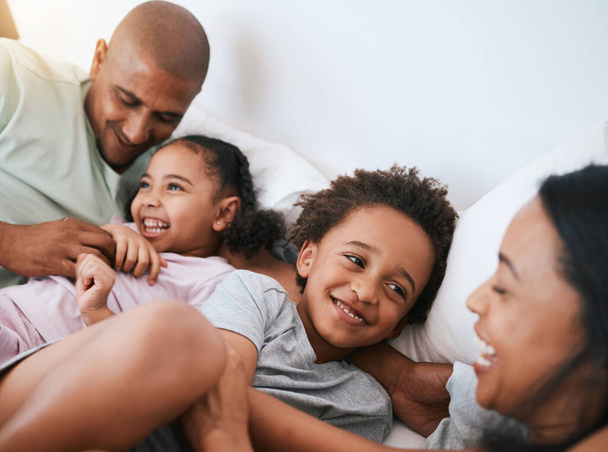Happy family, relax and playing in the morning on bed with smile for free time, weekend or fun holiday at home. Mother, father and children relaxing and laughing together for playful joy in bedroom. - Foto, Bild