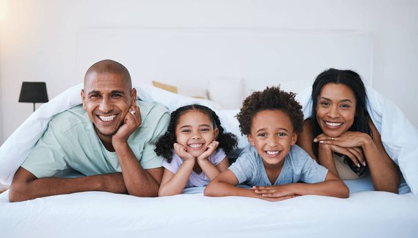 Portrait, family and smile in bedroom blanket in home, bonding and relaxing or lying. Bed, happiness and children with mother and father enjoying quality time together, having fun and care in house - Foto, imagen