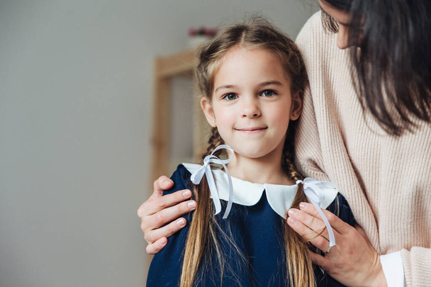 Mother embracing little content girl in dress and with braids looking at camera.  - Fotoğraf, Görsel