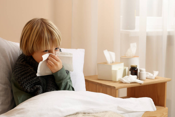 Boy blowing nose in tissue in bed at home. Cold symptoms - Foto, Imagen