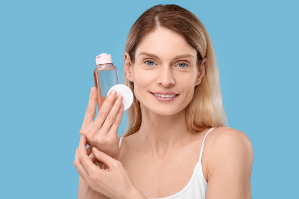 Beautiful woman with makeup remover and cotton pad on light blue background - Fotó, kép
