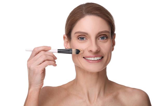 Woman applying foundation on face with brush against white background - Foto, Imagem