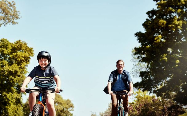 Er staat hen een leuke en zonnige dag te wachten. een jonge jongen en zijn vader rijden samen op hun fietsen - Foto, afbeelding