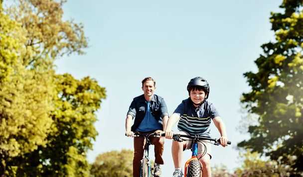 Genieten van een ritje met papa. een jonge jongen en zijn vader rijden samen op hun fietsen - Foto, afbeelding