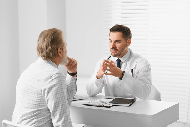 Doctor consulting senior patient at white table in clinic - Photo, Image