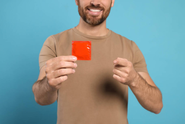Man holding condom on light blue background, closeup. Safe sex - Valokuva, kuva