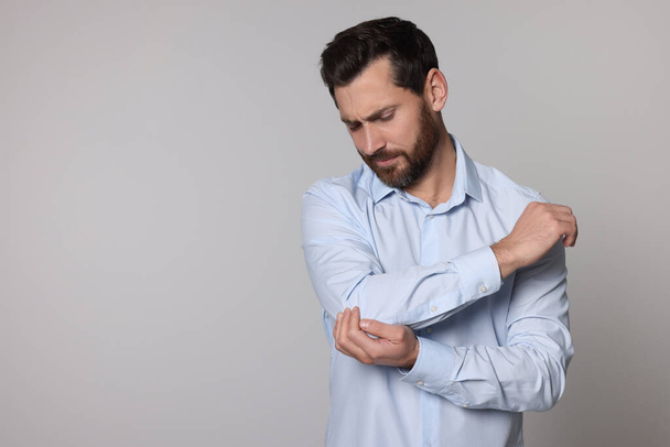 Man suffering from pain in his elbow on light background, space for text. Arthritis symptoms - Фото, изображение