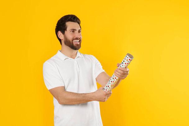 Happy man with party popper on yellow background. Space for text - Photo, Image