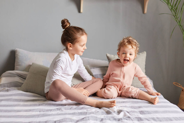 Children fun. Morning kid's leisure. Cute charming little girls playing in bedroom, sisters laughing on bed, expressing happiness, enjoying happy time. - Photo, Image